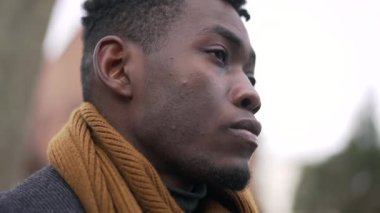 Serious black African man standing at park wearing winter clothing thinking about life