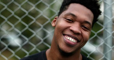 Smiling black guy leaning on metal fence standing casually outside