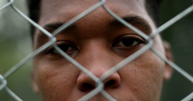 Serious African black man behind metal fence, close-up eyes staring camera