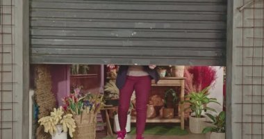 One female business woman sliding shutter door owner of flower store. Businesswoman of local shop opening store at sidewalk