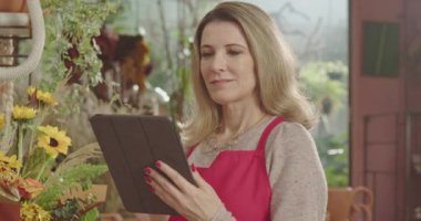 A happy middle aged female entrepreneur holding tablet smiling at camera using modern technology.