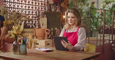 Female small business owner choosing bouquet flower for client talking with employee. Businesswoman using tablet device managing online orders