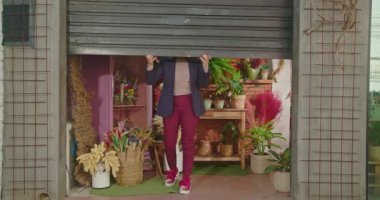 Person opening small business shop. Female entrepreneur owner of local flower store. Starting the day concept. Businesswoman sliding sidewalk shutter door