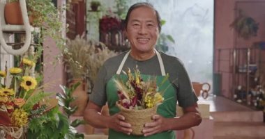 Portrait of an Asian American entrepreneur owner of local small business wearing apron plant. Flower shop business owner smiling at camera