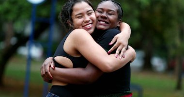 Çeşitli bayan arkadaşlar parkta birbirlerine sarılıyorlar. İki kız arkadaş kucaklaşır