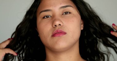 Latin asıllı sıradan bir kız kameraya bakıyor ve saçlarına dokunuyor. Kameraya bakan yakın plan kız yüzü, gerçek insan dizisi.