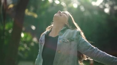 Carefree happy woman arms raised outside looking at sky feeling grateful. Person celebrating life standing in nature sunlight