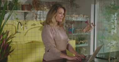 Female entrepreneur owner of retail store looking at laptop computer inside shop. A middle aged businesswoman checking online orders