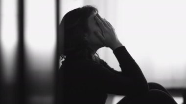 Monochromatic shot of desperate young woman suffering from emotional pain sitting on floor at home