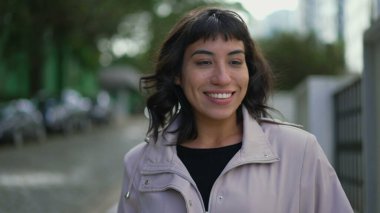 Happy young woman walking outside. One confident hispanic Brazilian girl walks outdoors in street smiling