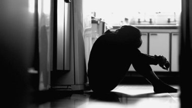 Depressed girl sitting on kitchen floor on monochrome. Black and white photography of woman in desperate moment