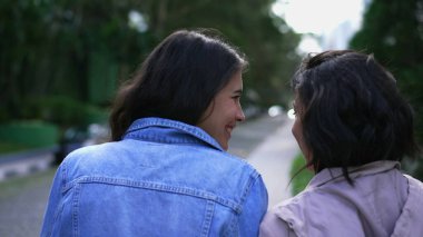 Back two young women walking outside together. Two female friends chatting