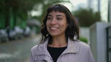 Happy young woman walking outside. One confident hispanic Brazilian girl walks outdoors in street smiling