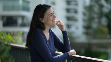 Happy woman standing home balcony thinking enjoying daylight. Pensive girl stand at apartment terrace
