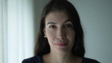 Portrait of woman in 30s with serious expression. Closeup face of person looking at camera standing by window