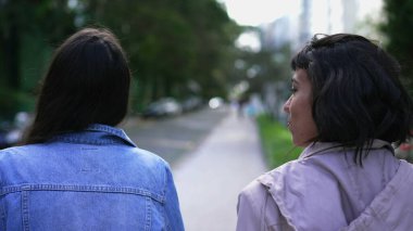 Back two young women walking outside together. Two female friends chatting