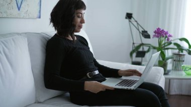 One hispanic latin girl opening computer laptop sitting at couch at elegant living room home