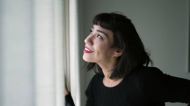 One beautiful hispanic girl looking out through curtain window checking sunlight day