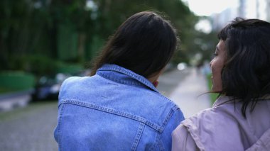 Back two young women walking outside together. Two female friends chatting