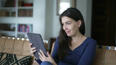 Happy woman browsing internet holding tablet at home living room. Person using modern digital device smiling at media content