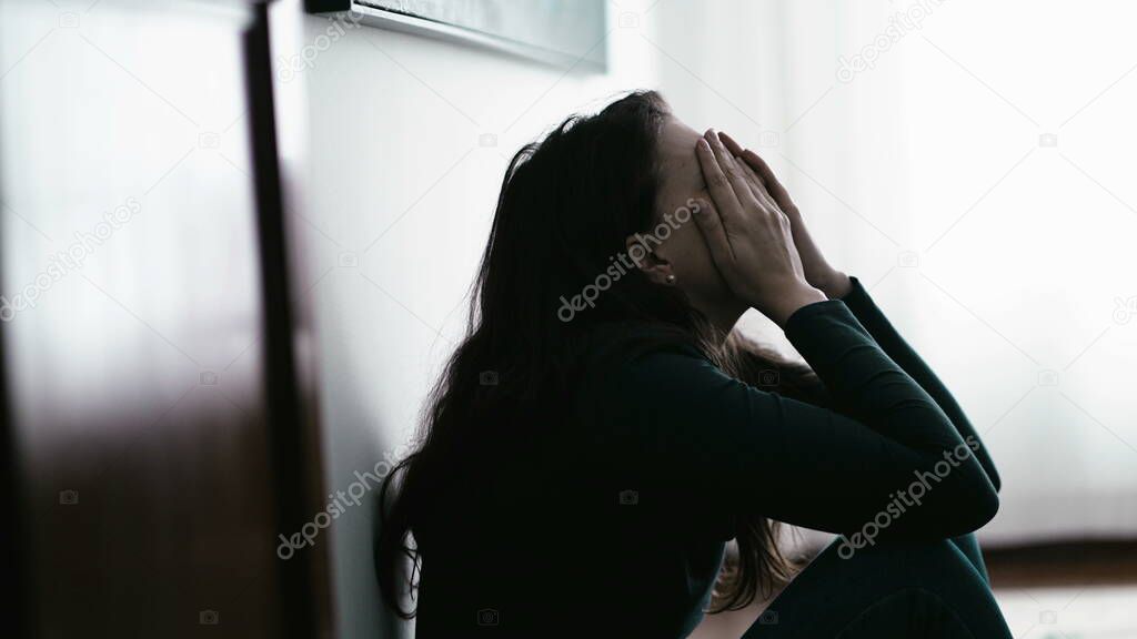 One desperate person suffering alone covering face with shame sitting on floor at home. Woman in emotional pain