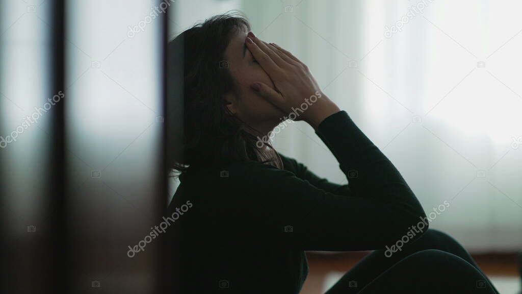 Depressed woman sitting on floor covering face with hands in despair