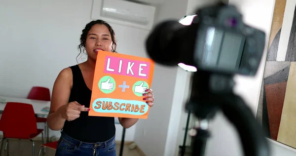 Millennial girl vlogger talking to camera showing sign for audience to like and subscribe to media channel