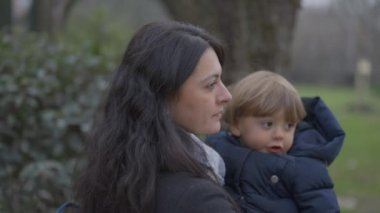Mother walking outside holding baby toddler in arms, mom kissing son in cheek
