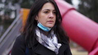 Pensive woman standing outside during covid with mask half on, circling around person