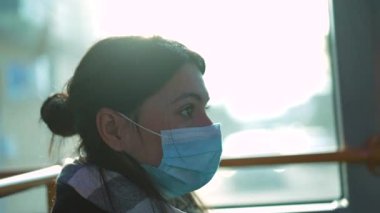 Commuter woman riding bus during pandemic wearing covid-19 face mask, looking out vehicle window