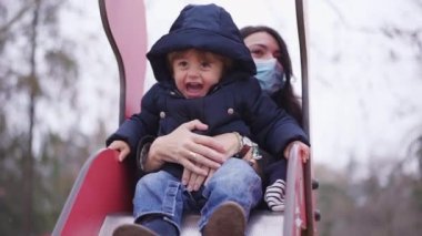 Baby toddler having fun at playground with mother during covid-19 winter season. Child sliding down tobogan