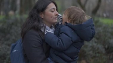 Mother and toddler boy walking outside at park. Mom kissing child in cheek