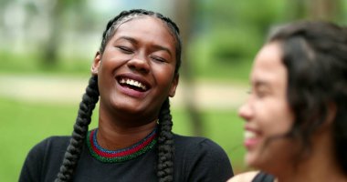Two diverse friends laughing and smiling together. Mixed race girlfriends talking in conversation outside. Authentic real life laugh and smile