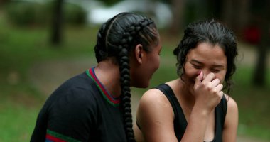 Two diverse friends laughing and smiling together. Mixed race girlfriends talking in conversation outside. Authentic real life laugh and smile