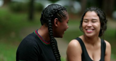 Two diverse friends laughing and smiling together. Mixed race girlfriends talking in conversation outside. Authentic real life laugh and smile