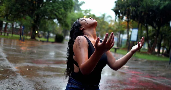 Spiritual young woman in rain shower raising arms, girl raising arms while raining