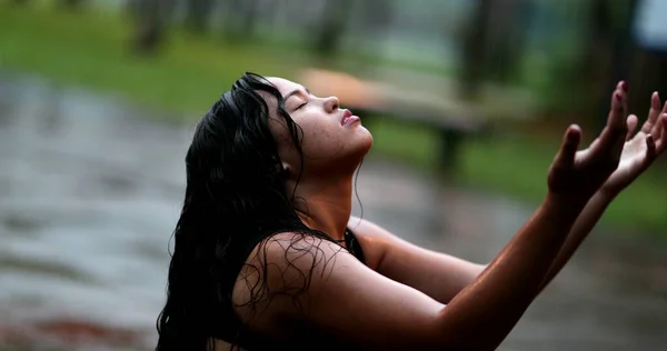 Spiritual young woman in rain shower raising arms, girl raising arms while raining