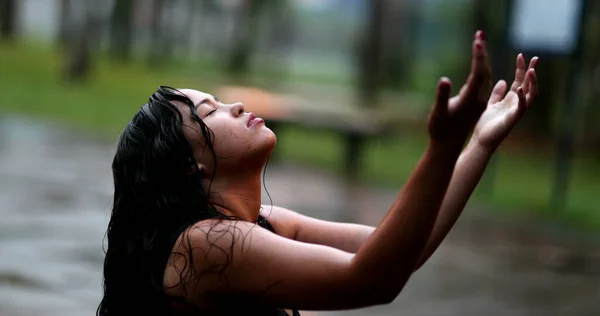 Spiritual young woman in rain shower raising arms, girl raising arms while raining