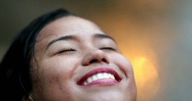 Yağmurda duran genç kadın gözleri kapalı gülümsüyor. Düşen damlaları hissederek hayattaki küçük şeylerden zevk alıyor.