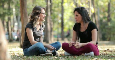 Candid friends seated at the park talking to each other Girlfriends speaking in conversation outdoors
