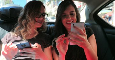 Candid friends in the back seat of a car checking their cellphone. Two girls looking at the smartphone