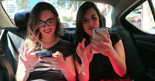 Candid friends in the back seat of a car checking their cellphone. Two girls looking at the smartphone