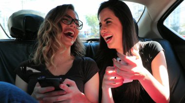 Friends real life laugh in the back seat of a car holding cellphone showing to friend screen