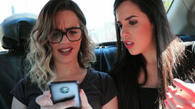 Friends concerned about what they are seeing on cellphone screen Girlfriends in the back seat of a car worried about content on smartphone screen