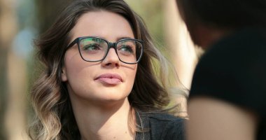 Candid Hispanic latin girl listening and talking to friend speak and interact in conversation outside in the park