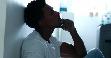 Pensive man sitting on kitchen floor feeling preoccupied thinking