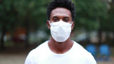 Black African person portrait face wearing surgical pandemic mask outside at park