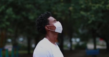 Person wearing surgical face mask pandemic prevention standing outside at park looking up