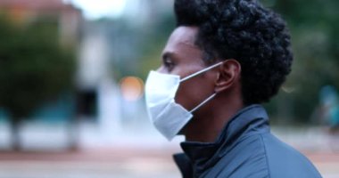 Black man wearing surgical medical face mask while walking forward in city outside