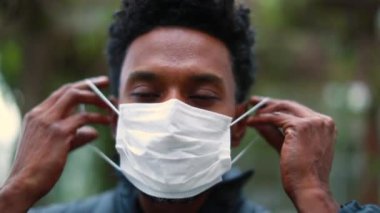 Black african man portrait putting pandemic mask prevention, person looking to camera wearing covid-19 mask